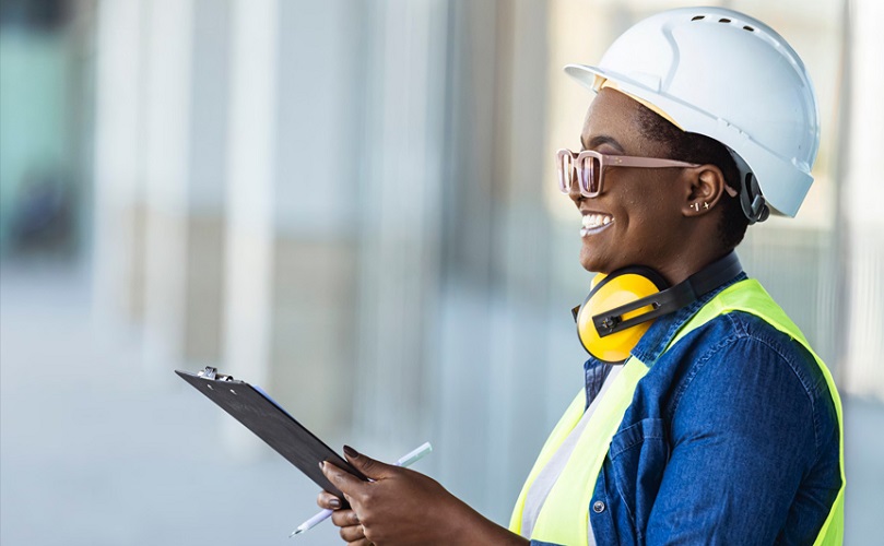 A person wearing a hard hat and earphones holding a clipboard