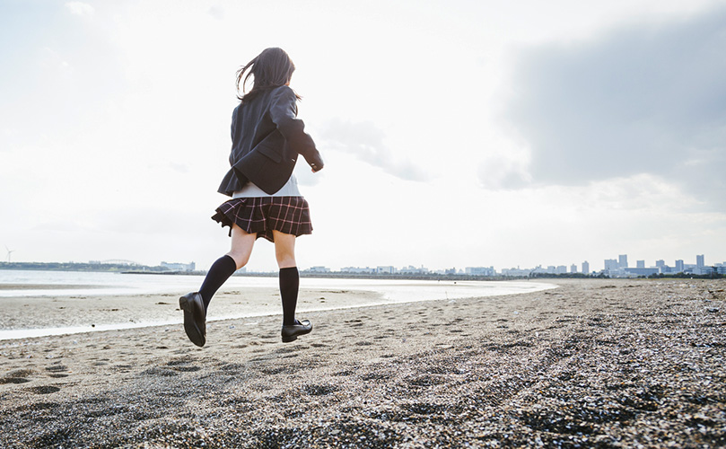 浜辺を走る女子高校生の写真