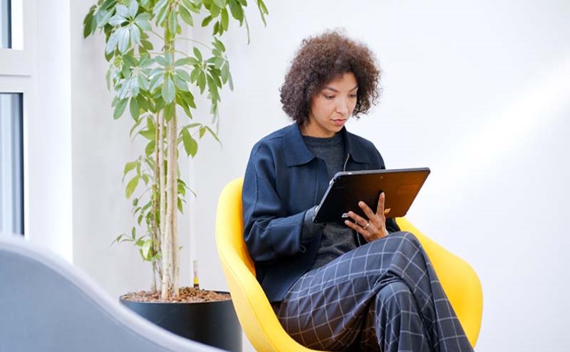 Una mujer sentada en una silla, mirando la tableta que tiene en la mano.