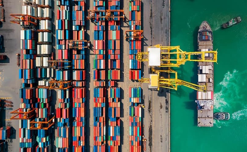 Aerial view of a port with a crane loading containers onto a ship, illustrating supply chain logistics.