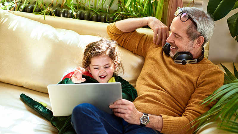 Mies ja lapsi istuvat sohvalla nauraen tietokonetta katsoessaan