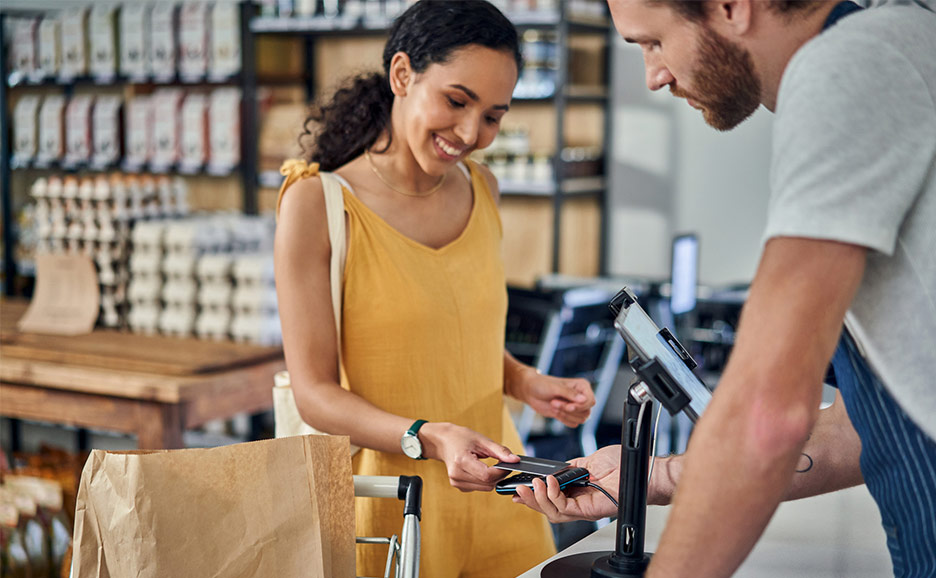 A young woman smiling while paying with a credit card at a supermarket.