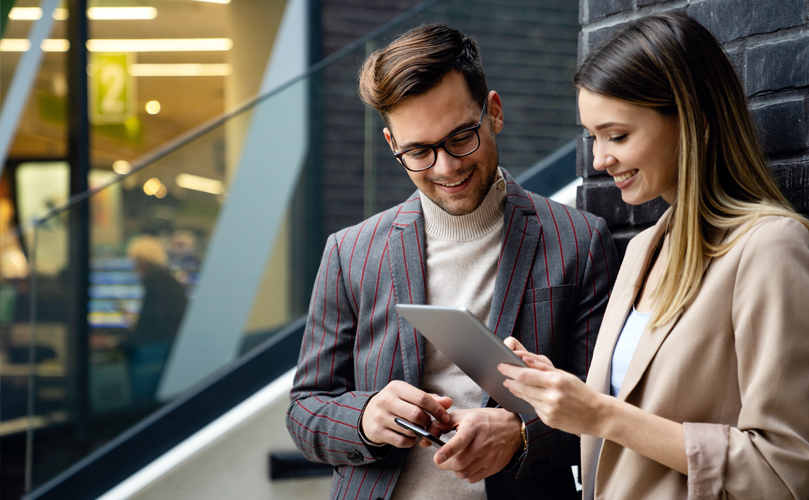 Two young business people stood looking at tablet in office setting