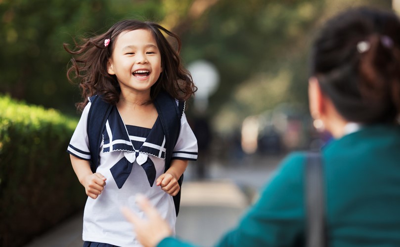 Happy girl in a school uniform running to a woman