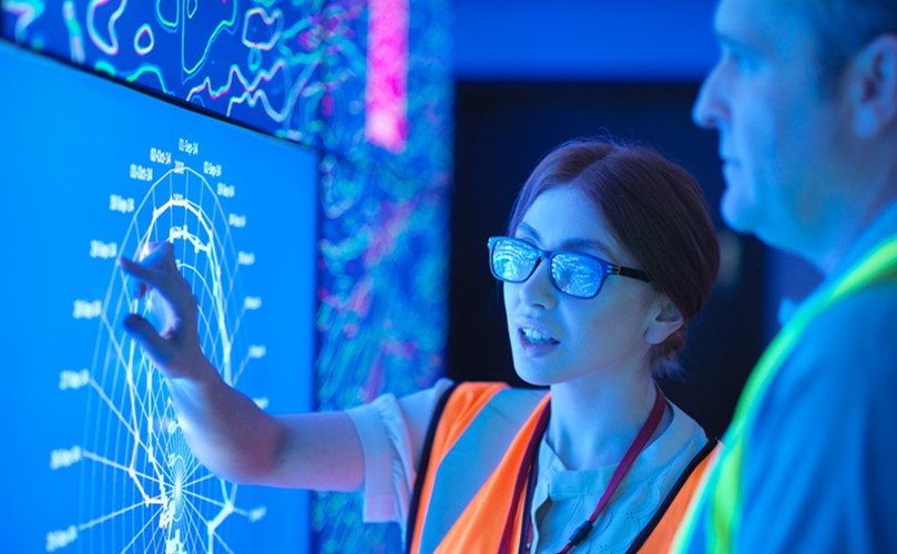 Female geologist with colleague studying graphical display of oil and gas bearing rock on screens