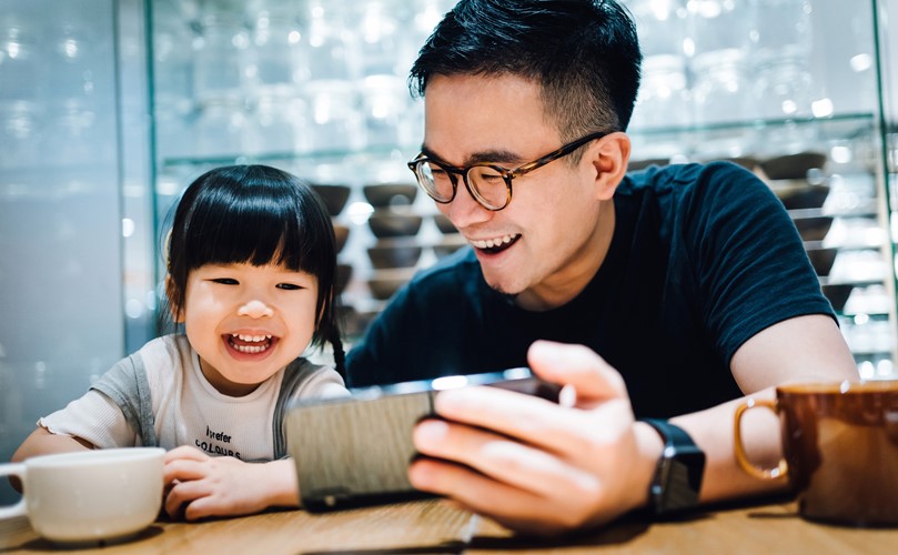 A person and a child sitting at a table using a mobile