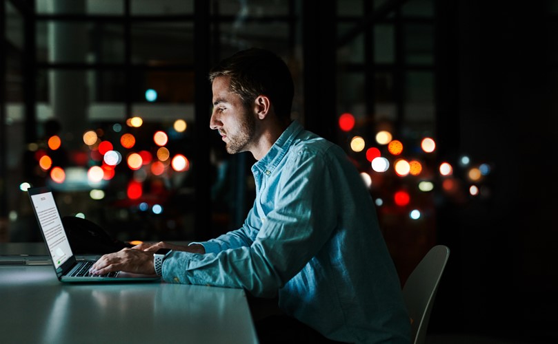 Young businessman in office at night typing on laptop