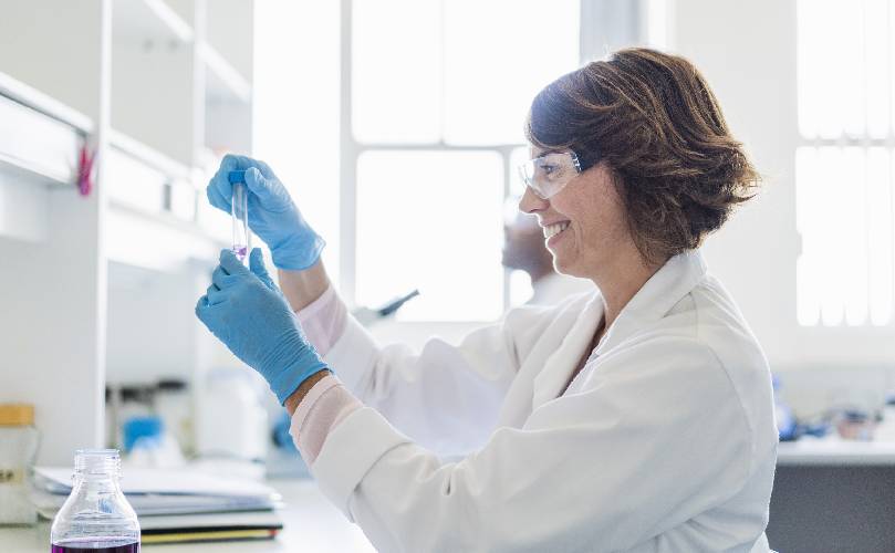  scientist working at a lab, wearing gloves and examining liquid in laboratory