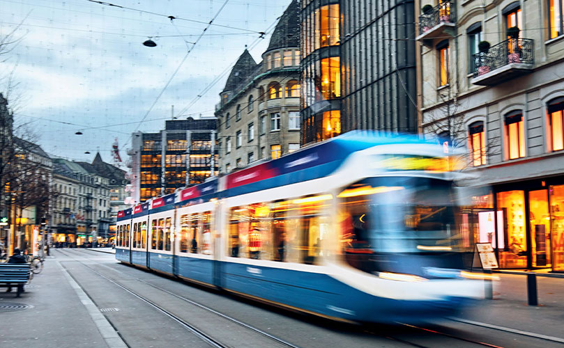 Blaue Straßenbahn fährt bei Dämmerung durch eine leere Stadtstraße