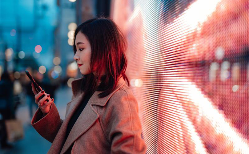 A woman stands confidently in front of a large screen displaying colorful graphics.