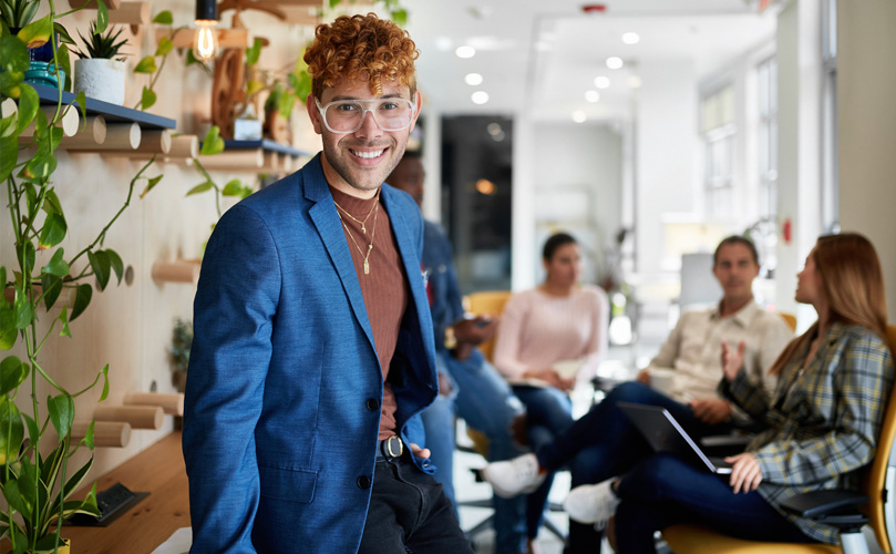 Ein Mann im blauen Blazer lächelt in einem gut beleuchteten Raum und strahlt eine freundliche und zugängliche Ausstrahlung aus.