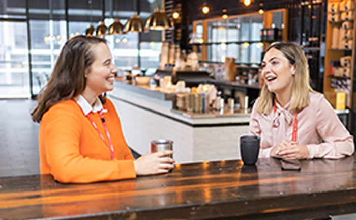 Two women engaged in conversation while sitting at a bar, enjoying drinks and each other's company.