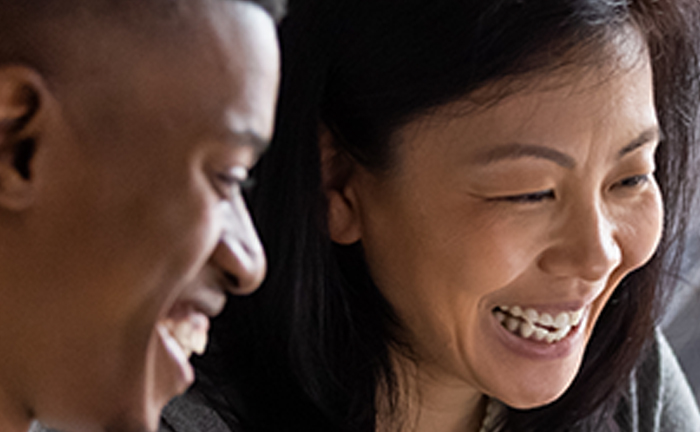 A man and woman smile at each other while looking at a laptop screen, sharing a moment of joy and connection.