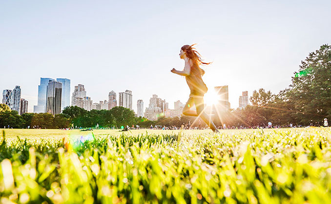 A woman runs in a sunlit park, with sunlight creating a warm glow behind her.