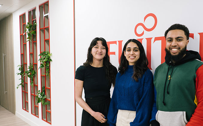 Three people stand in front of a wall displaying a prominent red sign