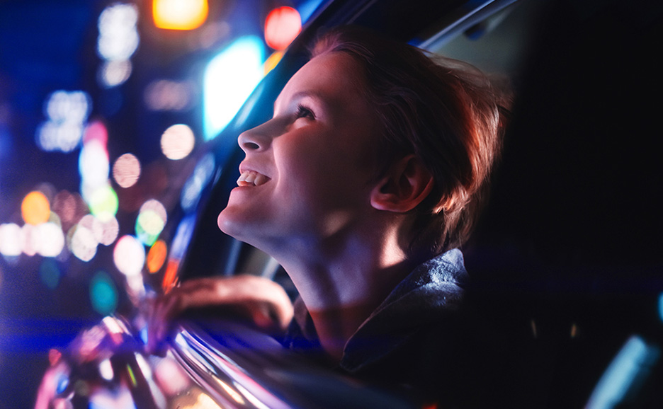 Image of a woman looking up and smiling from a car window at night