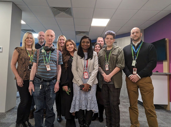 A diverse group of male and female Ability Matters members stood together in a office meeting room posing for a photo.