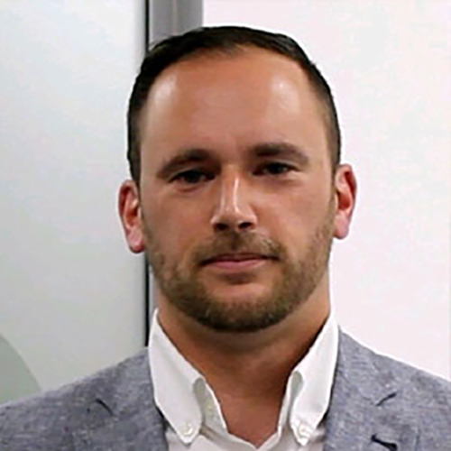 Jason Daniels, he is a white male with short brown hair. He wears a grey jacked and white shirt.