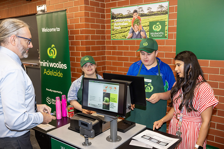 Two young people in green Woolworths uniforms practicing on a Fujitsu register. They are guided by a mentor.