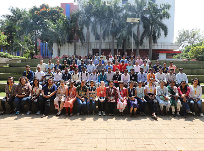 A large group of people sat on steps surronded by trees and greenery with a white building in the background. The people are visually impaired Indian students and members of Fujitsu Consulting India.