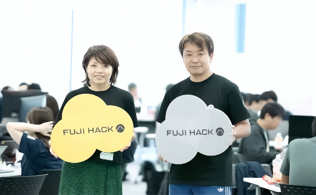 オフィスで「FUJI HACK」と書かれたロゴボードを掲げる男女2人。