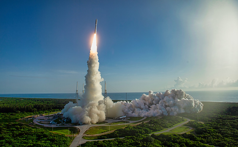 ロケット発射、打ち上げ時の轟音と煙。青い空と海を背景に、緑豊かな発射場