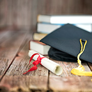卒業証書、角帽、本が積まれた木製の机
