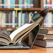 開いた本が置かれたノートパソコンと書棚の画像