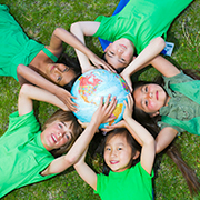 草原に寝そべり地球儀を囲む笑顔の子供たち