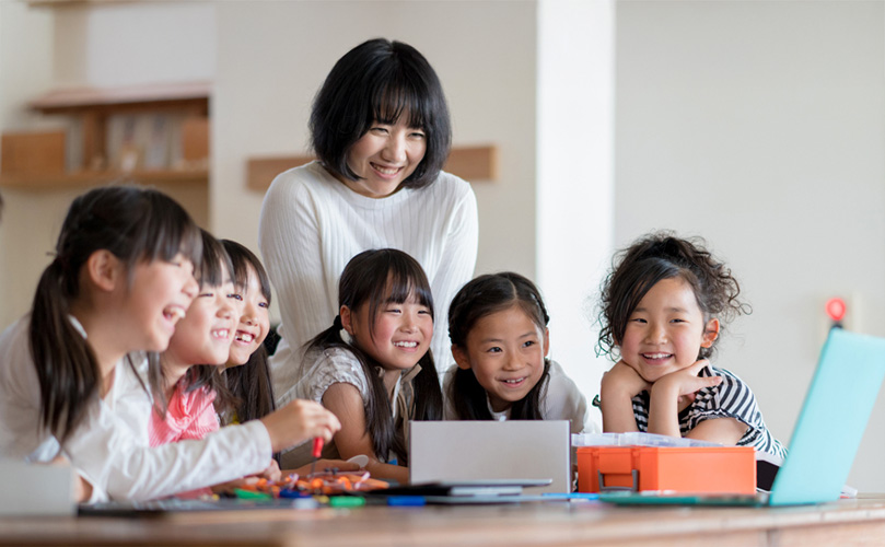 学習机に座って楽しそうに笑う子供たちと笑顔で見守る教師