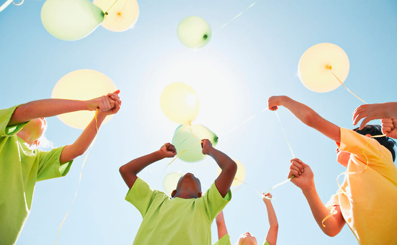 青い空の下、風船を飛ばしている子どもたちを下から見上げています