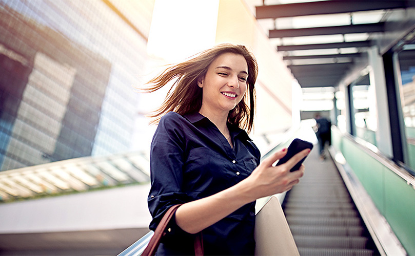 都会の街中でスマートフォンを見てほほ笑む女性