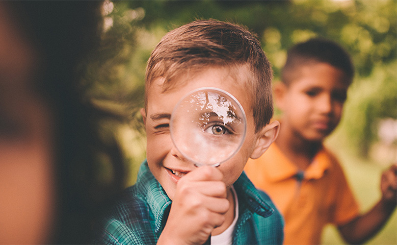 虫眼鏡をを通してこちらを見ているため片目が大きく見えている少年。