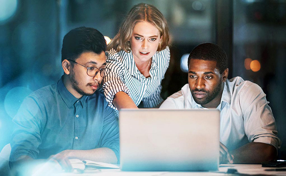 PCを囲んで夜遅くまで働く3人の多国籍なビジネスパーソン