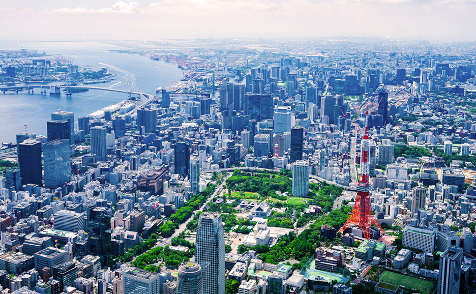 Luftaufnahme der Stadtlandschaft mit dem Tokyo Tower, umgeben von Hochhäusern und der Bucht von Tokio.
