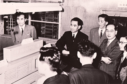 日本初の実用リレー式計算機「FACOM100」の画像　周りを取り巻くのは「日本のMr.コンピュータ」と呼ばれた富士通の技術者・池田敏雄、ノーベル物理学賞を受賞した湯川秀樹博士たち