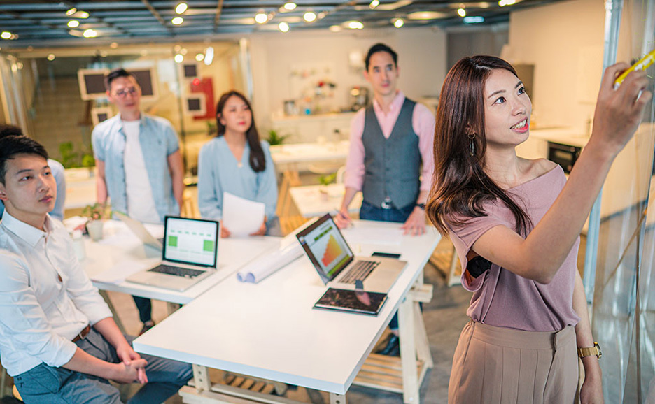 A woman presenting in an office, with her team members watching.