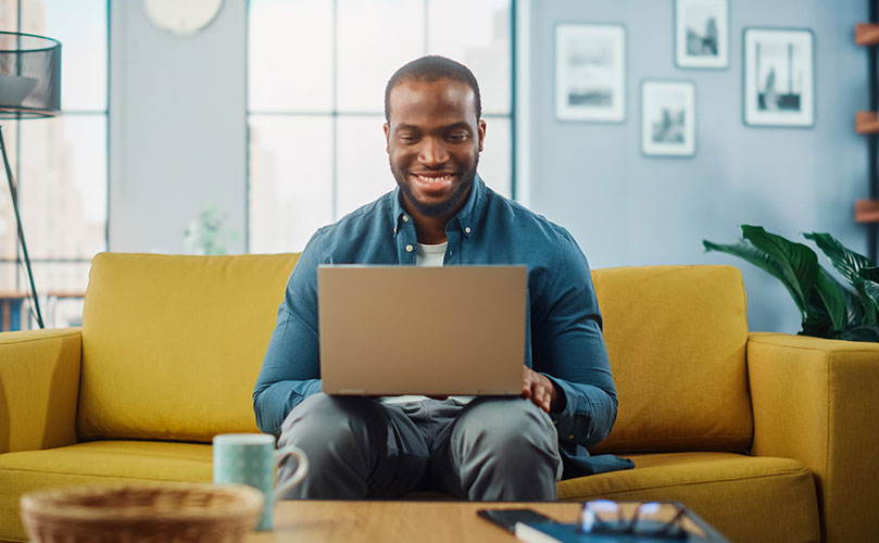 Smiling man using laptop on comfortable couch.