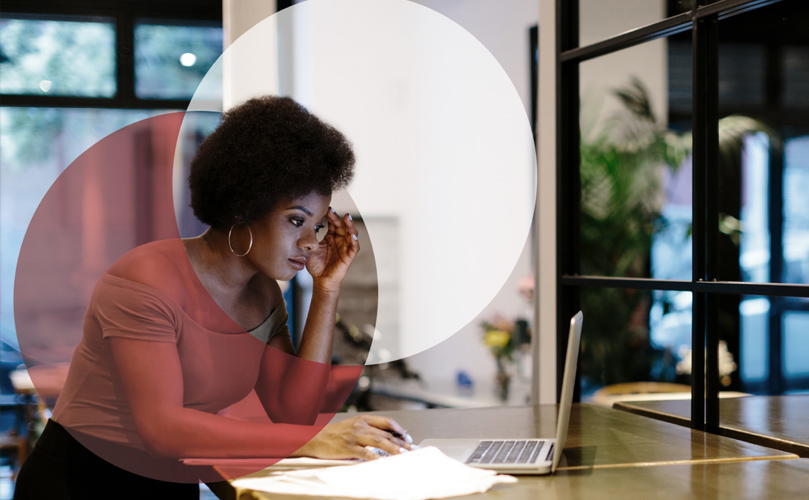 A woman working on a desk, looking pensively at computer and holding a pen