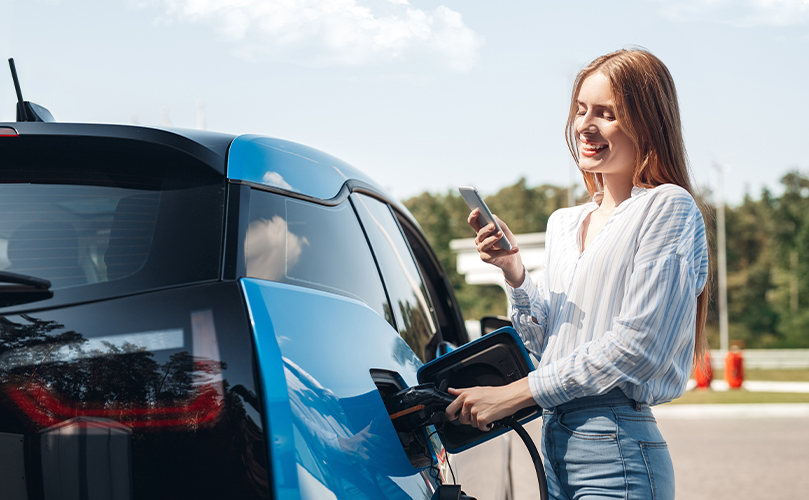 Una mujer riéndose de su teléfono mientras reabastece su coche