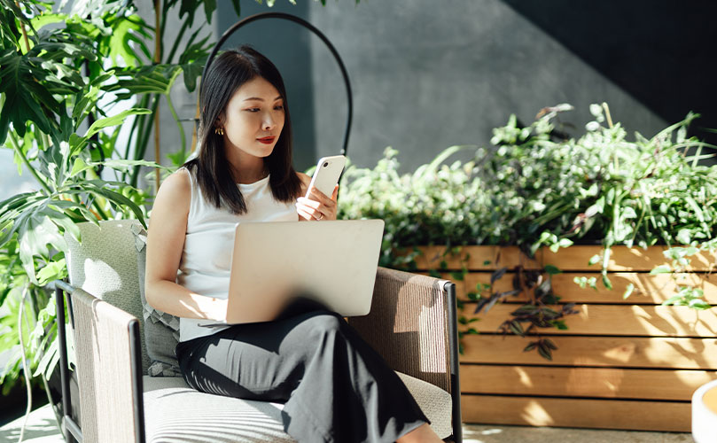 Eine Frau nutzt Laptop und Smartphone in einem Raum mit Zimmerpflanzen 