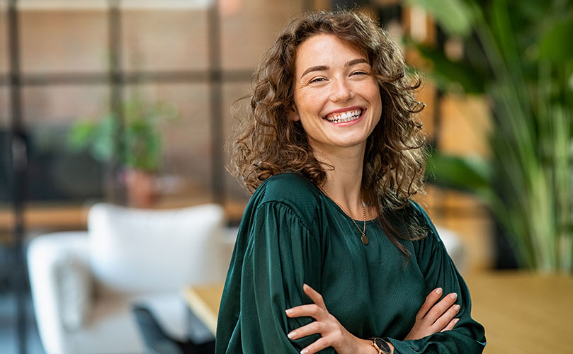 A woman smiling, standing with her arms crossed