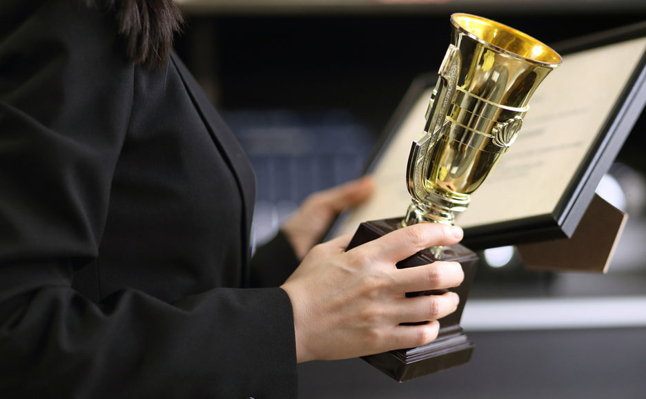 トロフィーと表彰状を持つ人物