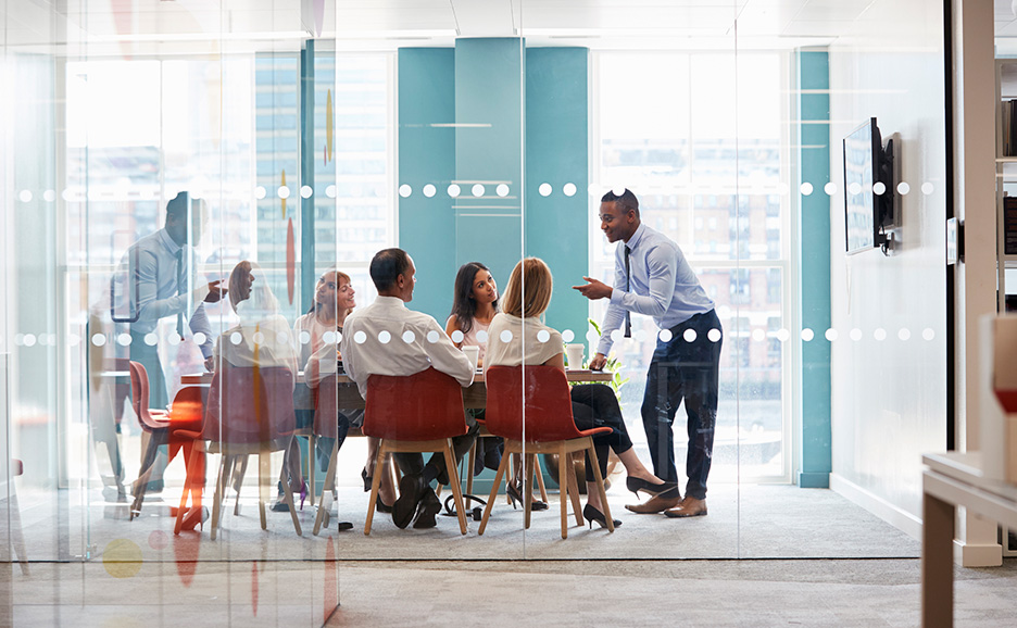 A businessman giving a presentation to participants in a glass-walled meeting room