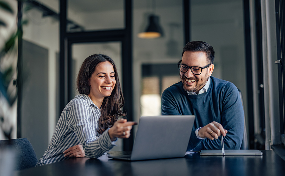 Two business people smiling and talking while pointing at a laptop screen