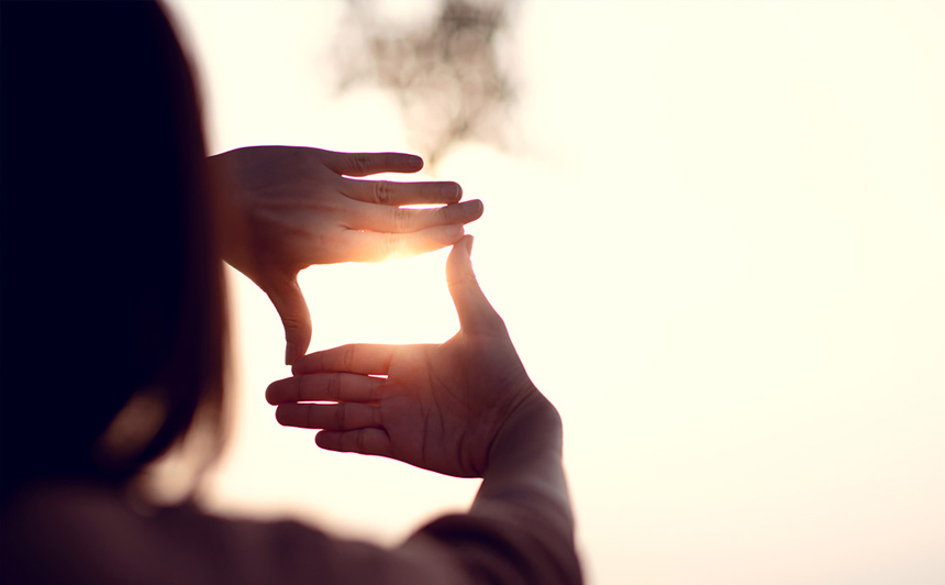 A person with their hands pointed to the sky, making a square, ensuring the sun is in the middle of the square