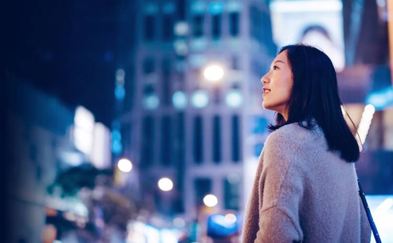 Une femme debout dans la rue regardant quelque chose hors du cadre contemplativement