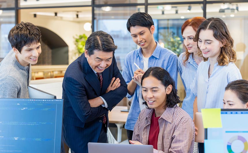 A group of people in an office setting looking at a computer and smiling