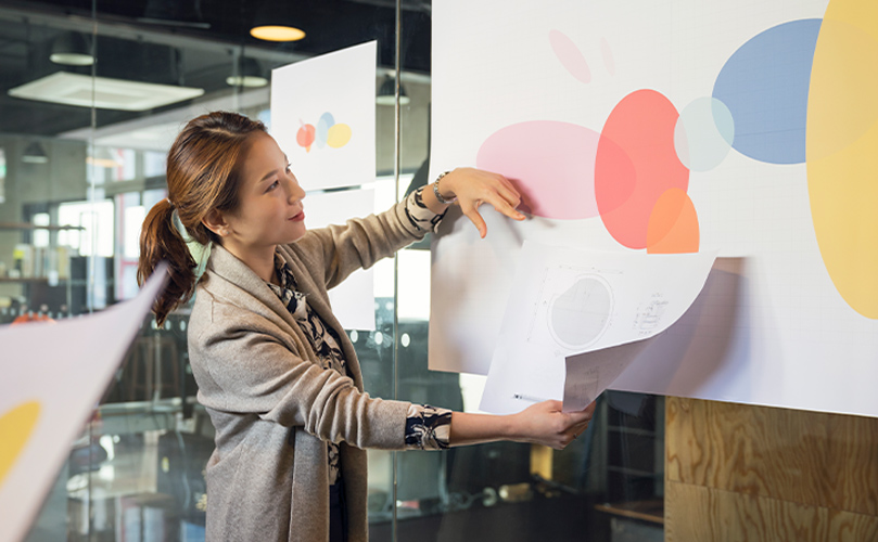 A woman holding papers while looking at a board