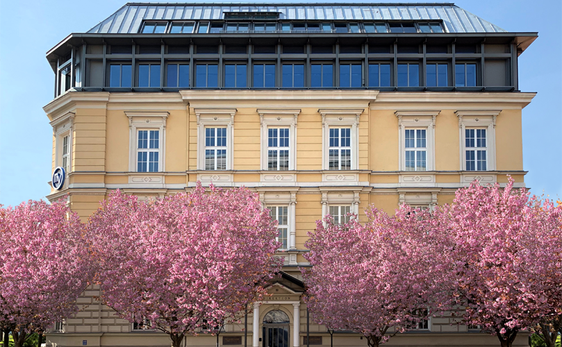 L'extérieur d'un bâtiment avec des arbres et des fleurs roses devant